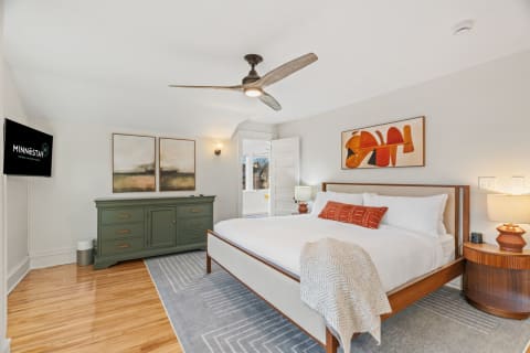 A cozy bedroom featuring a plush bed, abstract artwork, and warm wood accents.