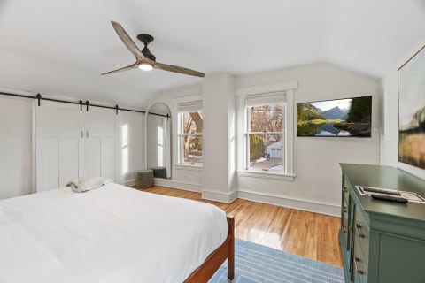 A modern bedroom featuring a white bed, hardwood floors, and large windows with natural light.