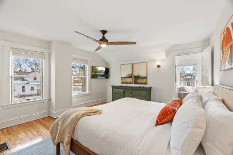 A modern bedroom with white linens, wooden floors, green dresser, and large windows overlooking a snowy landscape.