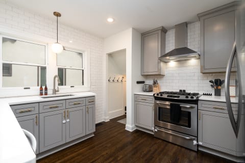 Stylish kitchen with gray cabinets and white tiles, featuring stainless steel appliances and a dark wooden floor.