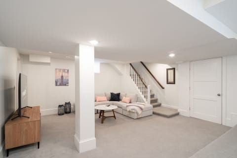 Contemporary basement living space featuring a sofa, TV, and staircase.