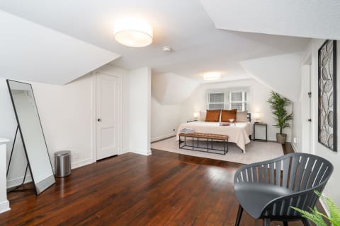 Modern bedroom with sloped ceiling, bed with brown pillows, and black bench.