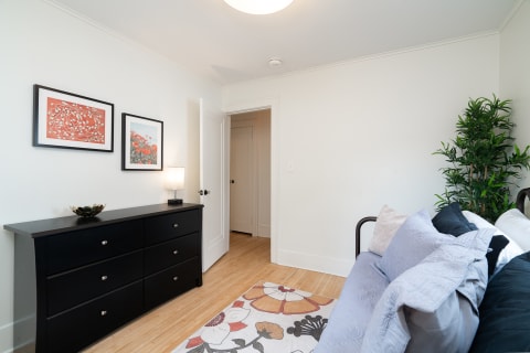 Bright and minimalist bedroom with a black dresser, framed artwork, and a daybed.