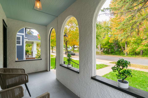 A view from a porch featuring arches, chairs, and vibrant autumn trees outside.