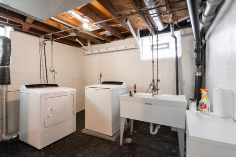 A functional basement laundry area featuring a washer, dryer, and sink amidst bright lighting.