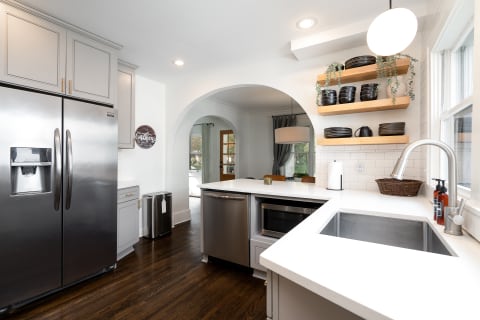 Contemporary kitchen featuring gray cabinets, a stainless steel fridge, and wooden shelves with black plates.