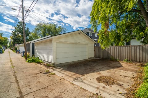 A white garage situated in an alley with trees and neighboring houses.
