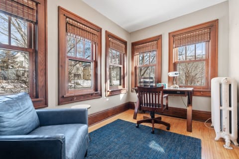 Home office corner with wooden windows, desk, and blue leather chair.