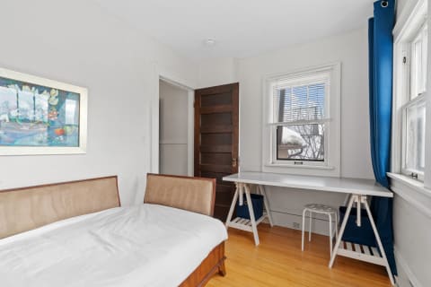 A bedroom with a bed, artwork on the wall, a desk, and natural light.