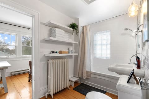 Modern bathroom with white tiled walls, vintage radiator, and plush towels on shelves.