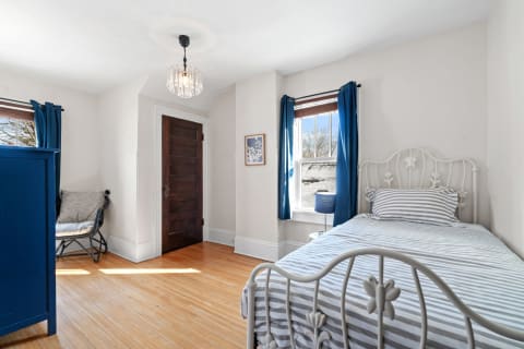 Cozy bedroom with a white metal bed, blue curtains, and wooden floor.