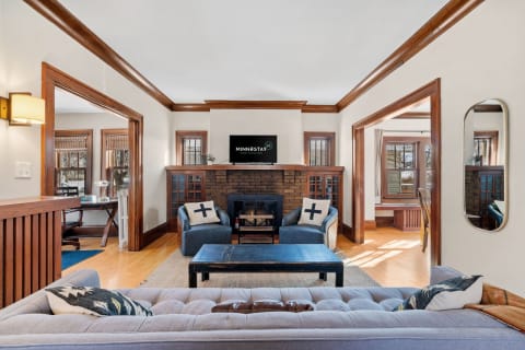 A cozy living room featuring a tufted gray sofa, blue armchairs with cross-pattern pillows, and a wooden coffee table in a well-lit space.