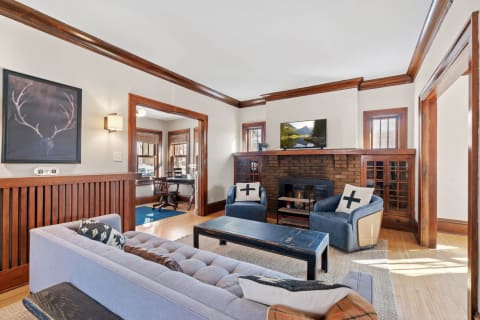 Inviting living room with a gray sofa, wooden fireplace, and large windows.