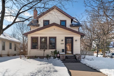 A two-story house with light siding and brown trim in a snowy setting.