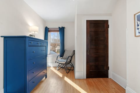 A corner of a room with a blue dresser, gray chair, and wooden door.