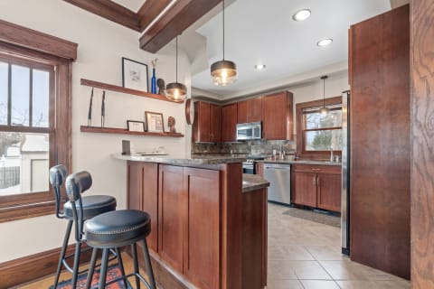 A kitchen featuring brown cabinetry, granite countertops, and bar stools with a snowy view outside.