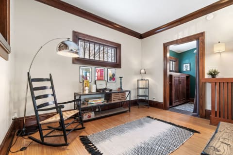 A living room featuring a black rocking chair, a modern floor lamp, a console table with a turntable, and colorful artwork on the walls.