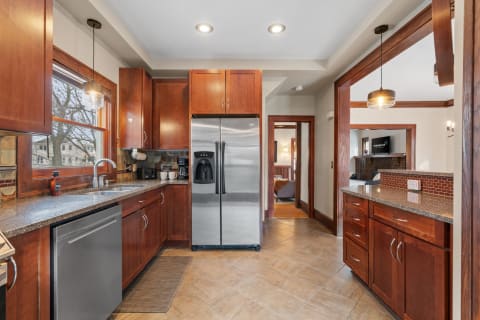 Interior of a modern kitchen with wooden cabinets, stainless steel appliances, and a sink under a large window.