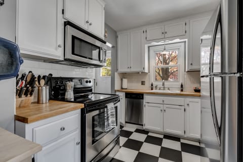 Bright kitchen with white cabinets, stainless steel appliances, and black and white tiled floor.