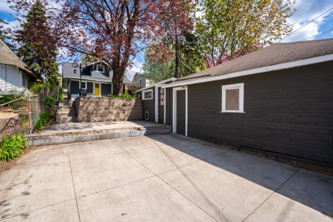 Outdoor area with a gray building, concrete driveway, and vibrant trees under a blue sky.