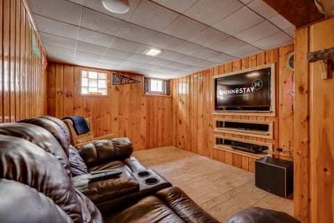 Interior view of a warm wooden-paneled basement with a leather couch and flat-screen television.