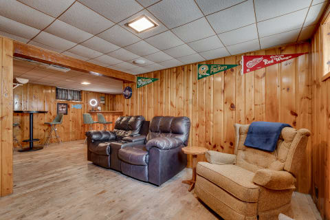 A comfortable basement lounge area with recliners, wooden table, and sports pennants.