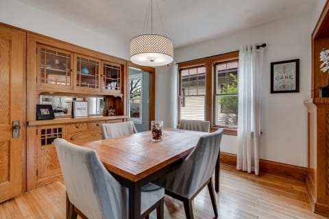 Dining room featuring a wooden table and upholstered chairs, with a sideboard and large windows.