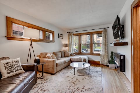 Living room with a beige sofa, dark leather chair, and large windows allowing natural light.