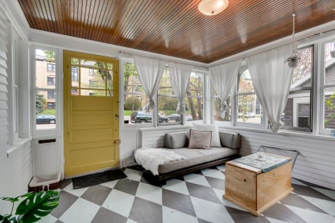 A bright sunroom with a yellow door, gray sofa, and diamond-patterned floor.