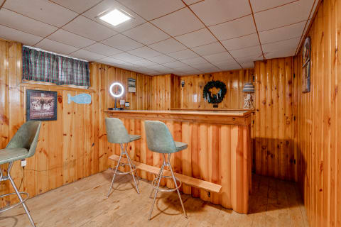 A wooden-paneled basement bar with two green stools and decorative wall items.