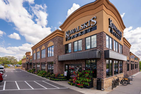 Exterior view of Kowalski's Market with flower arrangements and blue sky.