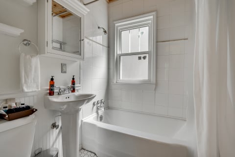 Bright, modern bathroom featuring a white pedestal sink, bathtub, and natural light from a window.