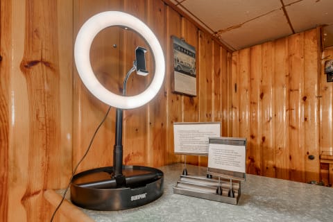 A ring light with a phone mount and instructional cards on a countertop, surrounded by wooden paneling.