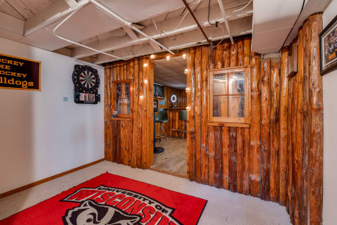 Cozy basement with wooden paneling, a dartboard, and a University of Wisconsin carpet.