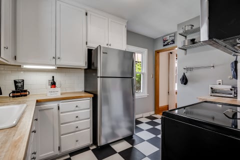 Modern kitchen with white cabinets, a stainless steel refrigerator, and checkered flooring.