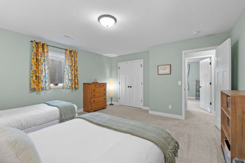 A bright bedroom with two twin beds, floral curtains, and a wooden dresser.