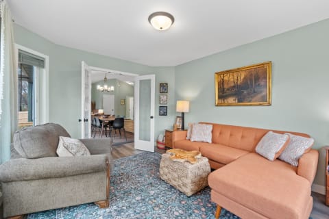 A well-decorated living room featuring an orange sectional sofa, gray armchair, and a dining area beyond.