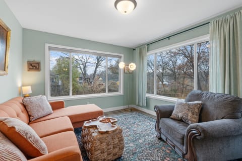 A cozy living room with a coral sectional sofa, blue area rug, and large windows letting in natural light.