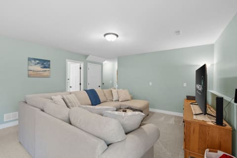 A light green-walled living room with a sectional sofa and a TV on a wooden console.