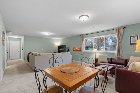 A cozy basement living area featuring a sectional sofa, loveseat, dining table, and soft lighting.