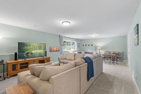 Spacious basement living area featuring a beige sectional sofa, a TV, and a small dining table.