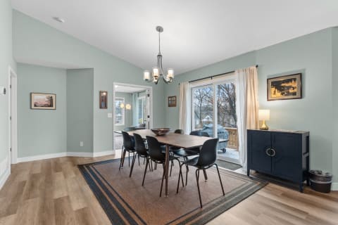 Dining room with a wooden table, black chairs, and a view of the outdoors through sliding glass doors.