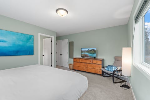 A modern bedroom with a light green color scheme, abstract blue art, and a wooden dresser with a TV.