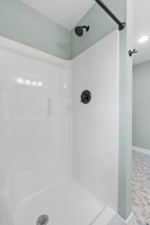 A contemporary shower stall featuring white walls and a mint green ceiling, with a black showerhead and control.