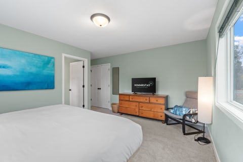 Cozy bedroom featuring light green walls, a blue abstract painting, a comfortable bed, and modern decor.