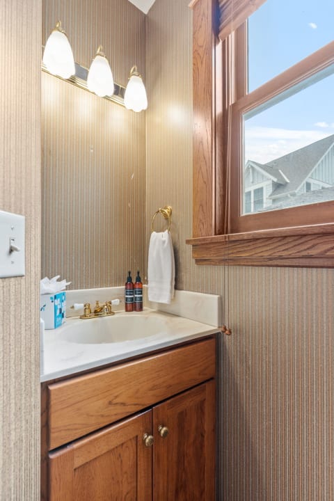 Powder room featuring a wooden vanity, gold fixtures, and striped wallpaper.