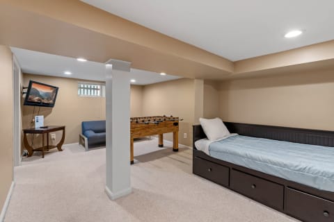 A recreation area with a foosball table, a blue couch, a wall-mounted TV, and a built-in bed with bedding.