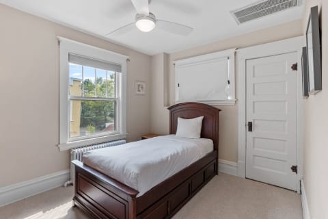 A cozy bedroom featuring a single bed, a ceiling fan, and a view outside from a large window.