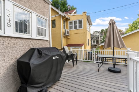 Outdoor deck with a BBQ grill, patio table with an umbrella, and neighborhood houses in the background.