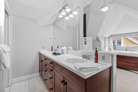A bright bathroom with a double vanity, white counters, wood cabinetry, and a view into an adjacent bedroom.